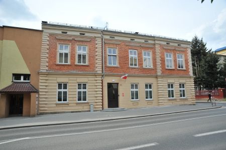 Ściana frontowa budynku przy ulicy Oświęcimskiej 20 w Chrzanowie po modernizacji. Ściana frontowa pomalowana na kolor ceglano- beżowy. Na wprost wejście główne.